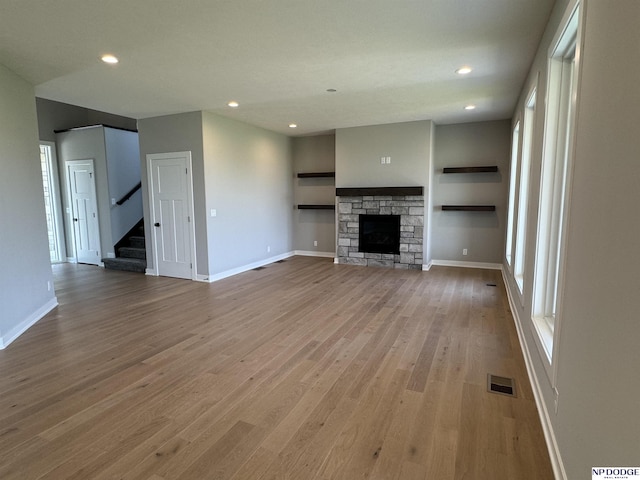 unfurnished living room featuring a stone fireplace, a wealth of natural light, and hardwood / wood-style flooring