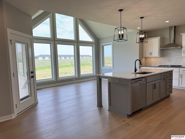 kitchen featuring dishwasher, a center island with sink, sink, wall chimney exhaust hood, and decorative light fixtures