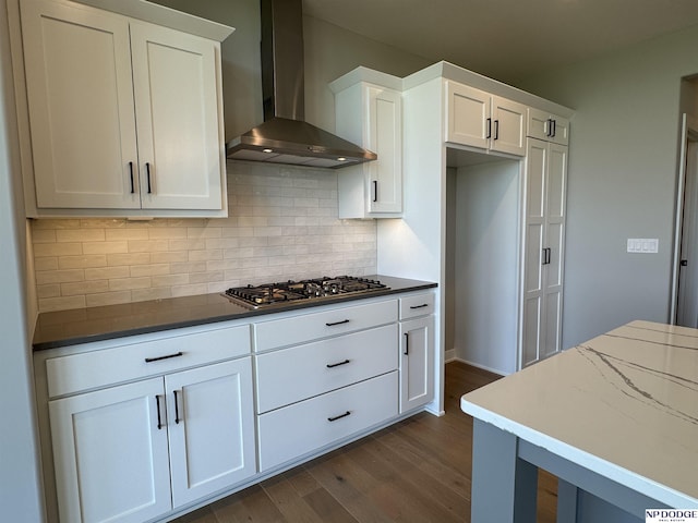 kitchen featuring stainless steel gas stovetop, white cabinetry, wall chimney range hood, and backsplash