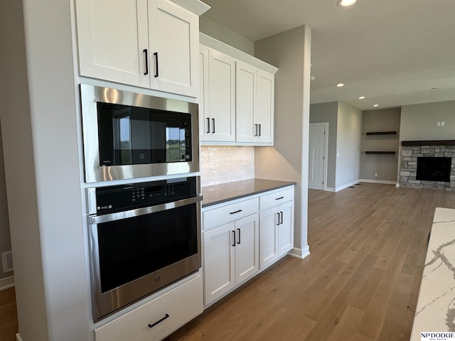 kitchen featuring white cabinetry, built in microwave, a stone fireplace, oven, and decorative backsplash