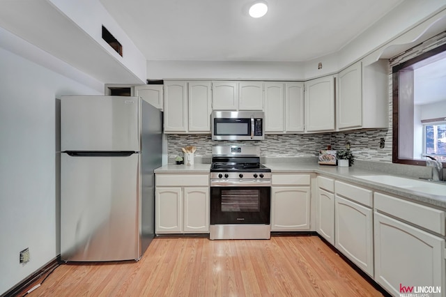 kitchen featuring tasteful backsplash, stainless steel appliances, sink, light hardwood / wood-style floors, and white cabinetry