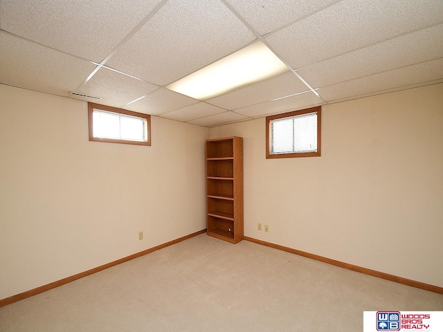 basement with a paneled ceiling and light carpet