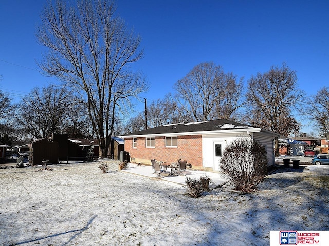 snow covered back of property featuring a patio