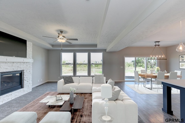 living room featuring a textured ceiling, ceiling fan with notable chandelier, a raised ceiling, and a fireplace