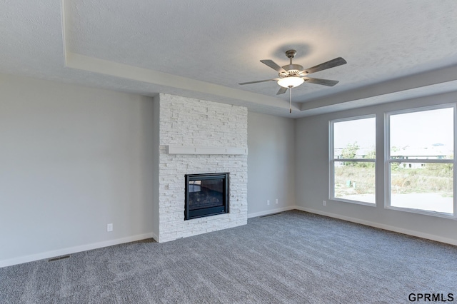 unfurnished living room featuring carpet, ceiling fan, a fireplace, and a tray ceiling