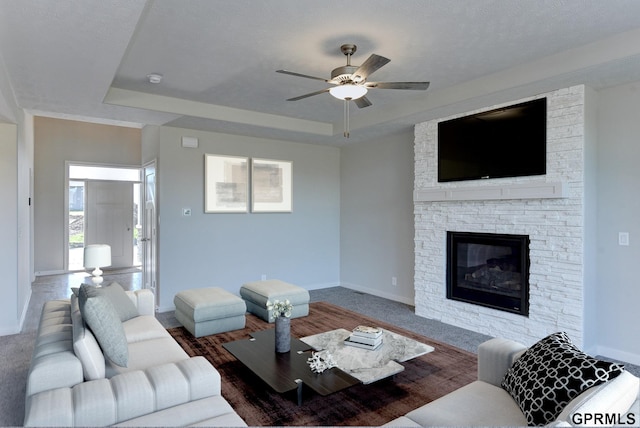 living room with carpet, a raised ceiling, ceiling fan, and a stone fireplace