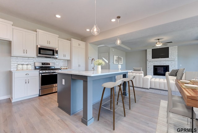 kitchen with decorative backsplash, stainless steel appliances, white cabinetry, hanging light fixtures, and an island with sink