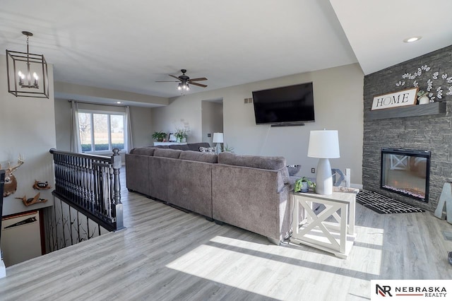 living room featuring ceiling fan with notable chandelier, light wood-type flooring, and a stone fireplace