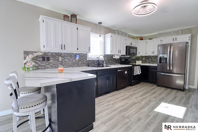 kitchen featuring light wood-type flooring, sink, black appliances, decorative light fixtures, and white cabinetry