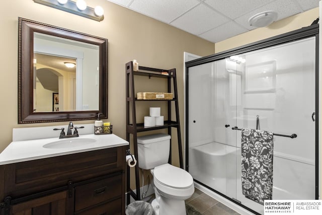 bathroom with an enclosed shower, a drop ceiling, toilet, and vanity