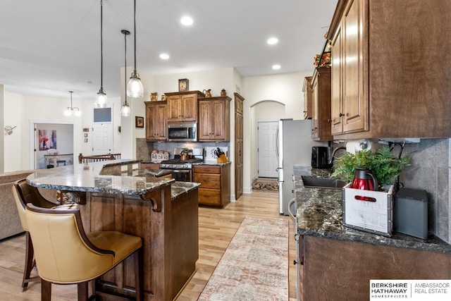 kitchen with a breakfast bar, light hardwood / wood-style flooring, dark stone countertops, decorative light fixtures, and stainless steel appliances