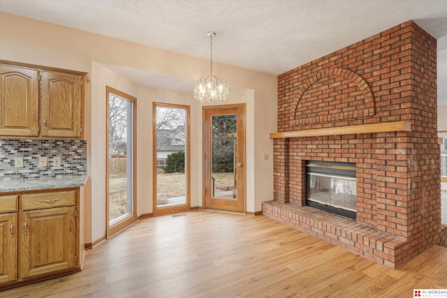 unfurnished living room featuring a fireplace, light wood-type flooring, a textured ceiling, and an inviting chandelier