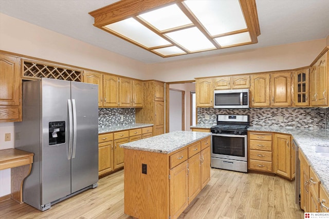 kitchen with light hardwood / wood-style floors, tasteful backsplash, a kitchen island, light stone counters, and stainless steel appliances