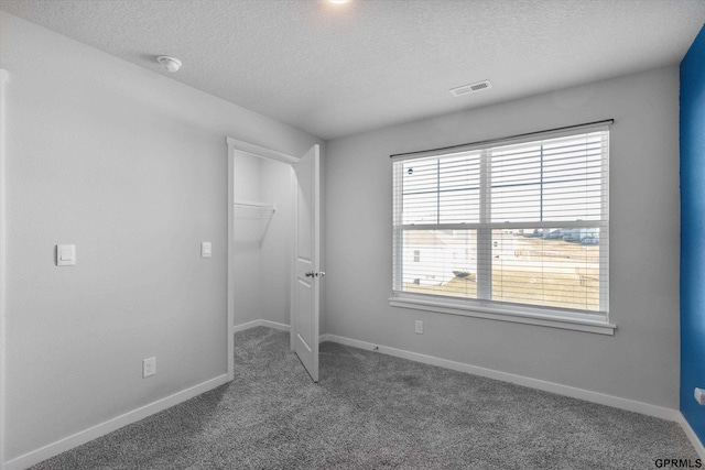 unfurnished bedroom with a walk in closet, a textured ceiling, dark carpet, and a closet