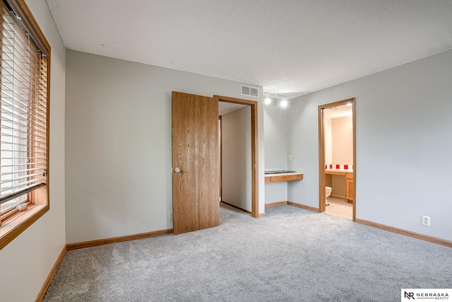 unfurnished bedroom with light colored carpet, a textured ceiling, and ensuite bathroom