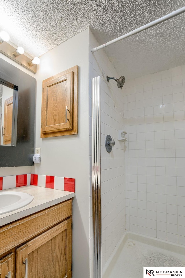 bathroom with a textured ceiling, vanity, and a tile shower