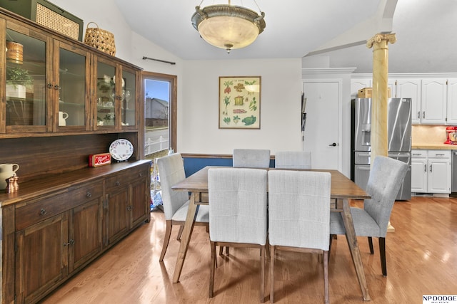 dining space featuring light wood-type flooring, decorative columns, and vaulted ceiling