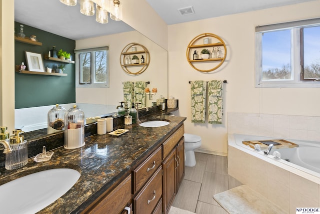 bathroom with tiled tub, vanity, and toilet