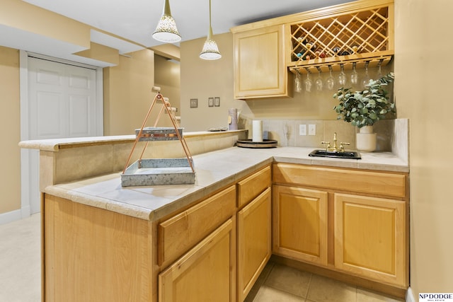 kitchen featuring kitchen peninsula, tasteful backsplash, sink, light tile patterned floors, and hanging light fixtures