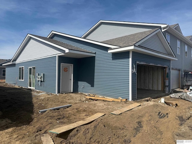 view of front of property featuring dirt driveway, an attached garage, and a shingled roof