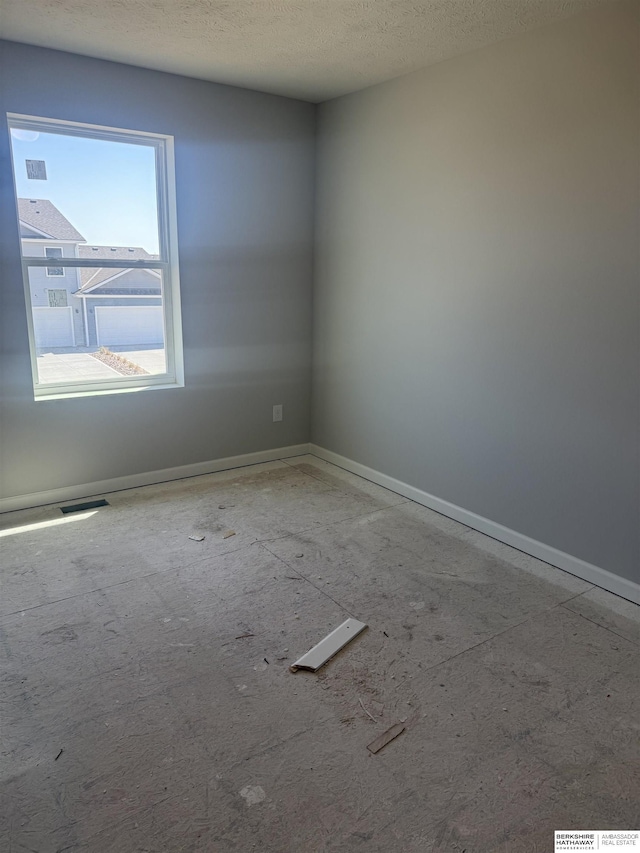 spare room featuring a textured ceiling, visible vents, and baseboards