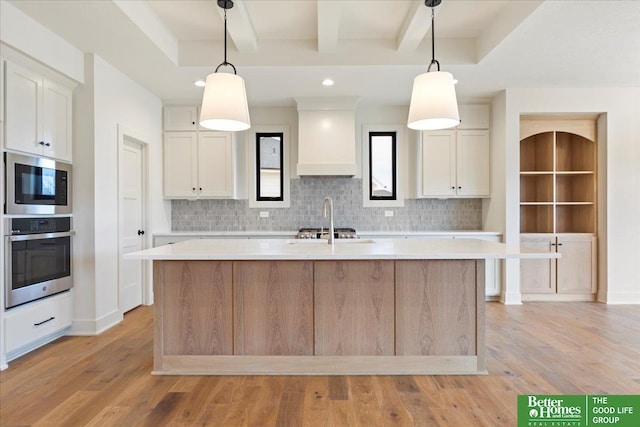 kitchen featuring pendant lighting, premium range hood, white cabinets, an island with sink, and appliances with stainless steel finishes