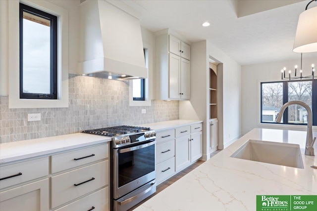 kitchen featuring high end range, white cabinets, sink, hanging light fixtures, and wall chimney exhaust hood