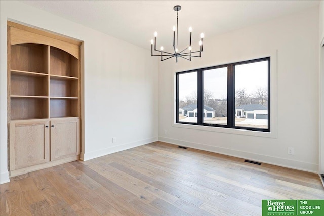 unfurnished dining area with a notable chandelier, built in shelves, and light hardwood / wood-style flooring