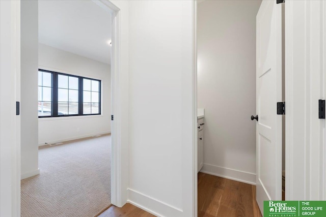 corridor with carpet floors, wood finished floors, visible vents, and baseboards