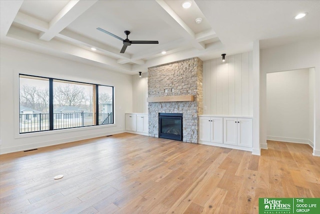 unfurnished living room featuring coffered ceiling, ceiling fan, beam ceiling, light hardwood / wood-style floors, and a stone fireplace