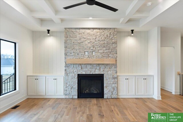 unfurnished living room with beamed ceiling, a healthy amount of sunlight, a stone fireplace, and coffered ceiling