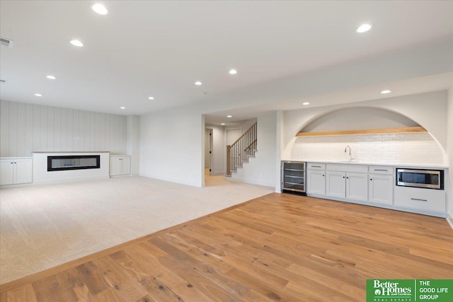 unfurnished living room with recessed lighting, a glass covered fireplace, a sink, light wood-type flooring, and beverage cooler