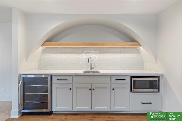 bar with wine cooler, wood finished floors, a sink, tasteful backsplash, and stainless steel microwave