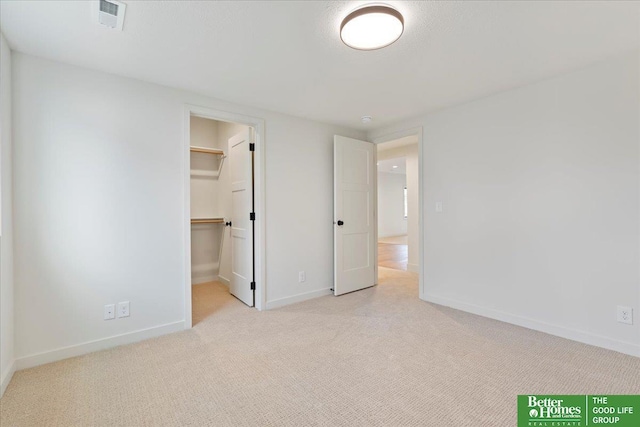 unfurnished bedroom featuring a walk in closet, light carpet, visible vents, and baseboards