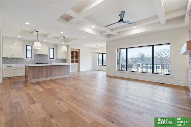 kitchen with a center island with sink, light countertops, hanging light fixtures, open floor plan, and white cabinetry