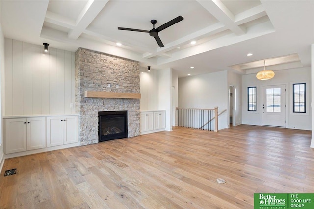 unfurnished living room featuring visible vents, coffered ceiling, a stone fireplace, light wood-style floors, and beam ceiling