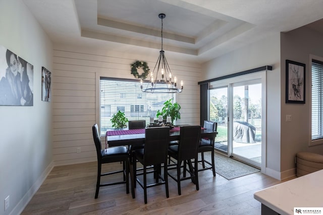 dining room with hardwood / wood-style floors, a tray ceiling, an inviting chandelier, and wooden walls