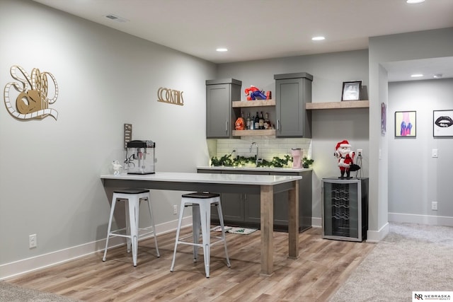 bar featuring sink, wine cooler, light hardwood / wood-style flooring, decorative backsplash, and gray cabinets