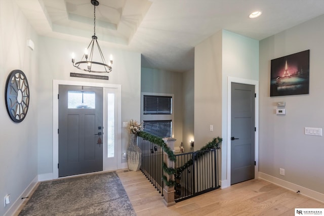 entrance foyer featuring a chandelier, light wood-type flooring, and a raised ceiling