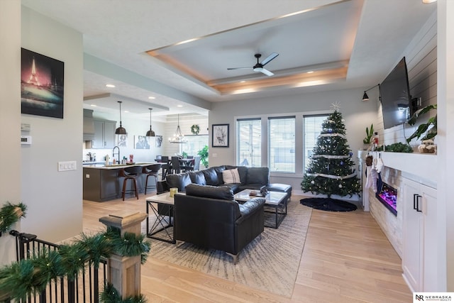 living room featuring ceiling fan, light wood-type flooring, sink, and a tray ceiling