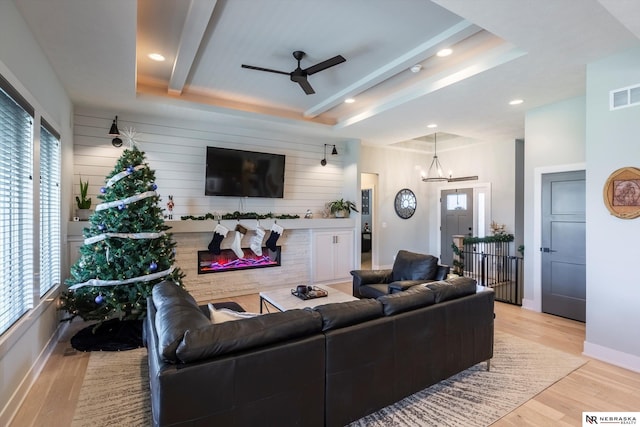 living room featuring a tray ceiling, wooden walls, ceiling fan with notable chandelier, and light wood-type flooring