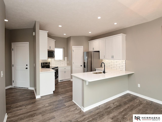 kitchen featuring sink, dark hardwood / wood-style flooring, kitchen peninsula, white cabinets, and appliances with stainless steel finishes