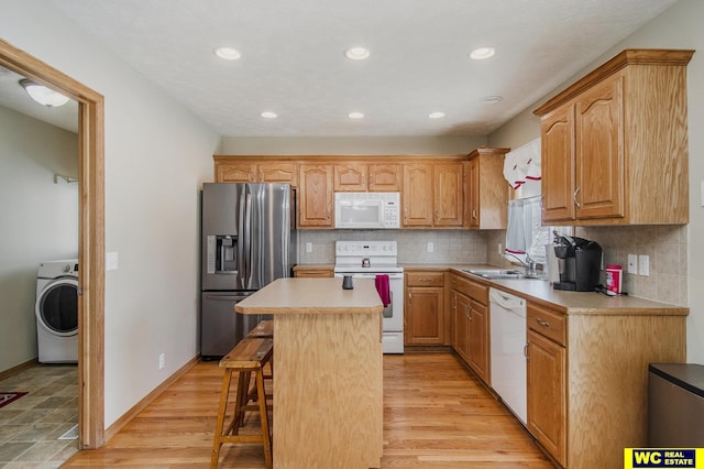 kitchen with white appliances, sink, a kitchen island, a kitchen bar, and washer / clothes dryer