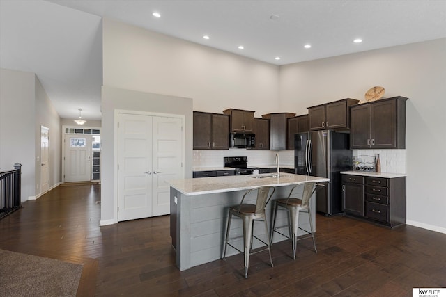 kitchen with black appliances, a breakfast bar, a center island with sink, and tasteful backsplash