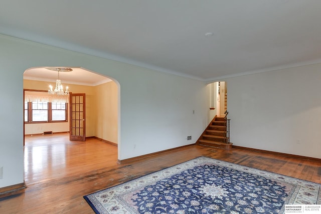 empty room featuring an inviting chandelier, ornamental molding, and hardwood / wood-style flooring