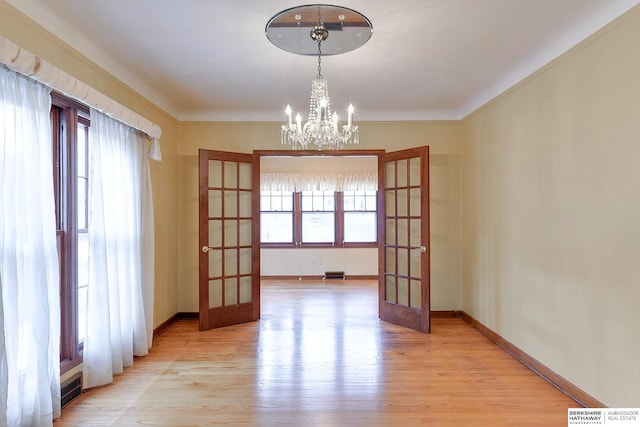 unfurnished dining area featuring an inviting chandelier, light wood-type flooring, and french doors