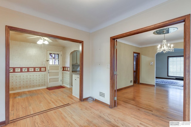 empty room featuring ceiling fan with notable chandelier, a healthy amount of sunlight, and light wood-type flooring