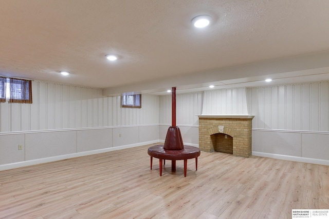 basement with light hardwood / wood-style flooring and a brick fireplace