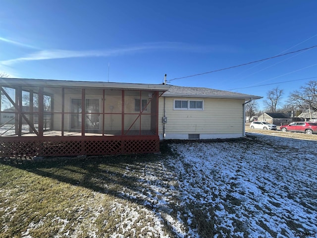 snow covered rear of property featuring a sunroom and a lawn