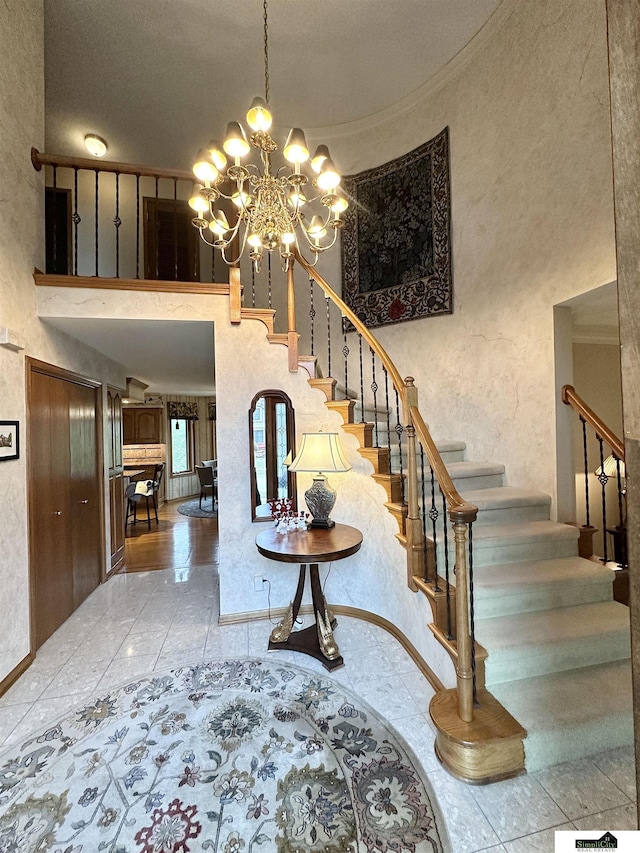 stairs with ornamental molding, a high ceiling, and a chandelier